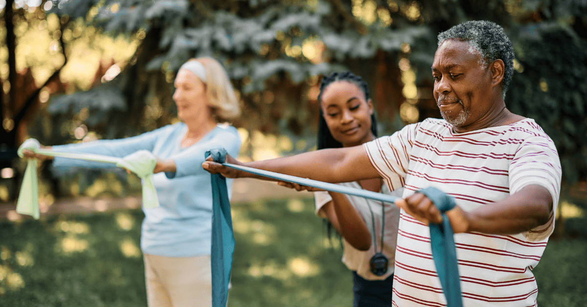 older adult man and woman using exercise bands outside with a trainer